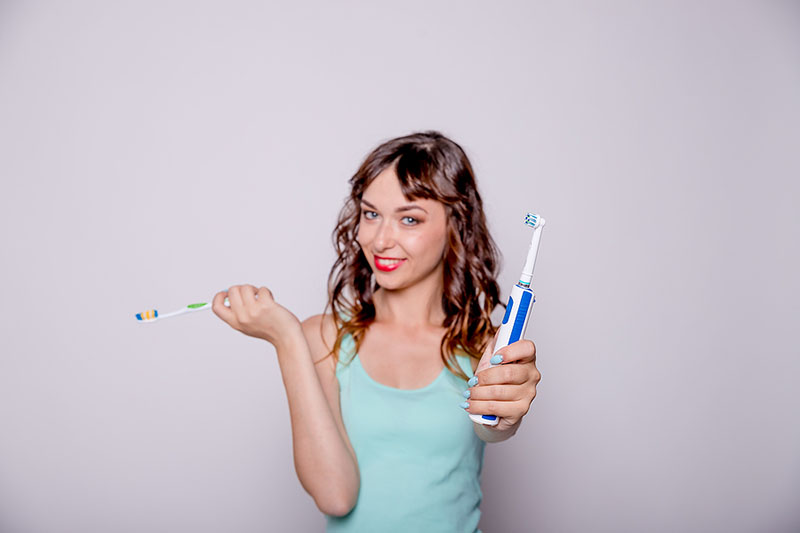 Woman holding electric and manual toothbrushes.