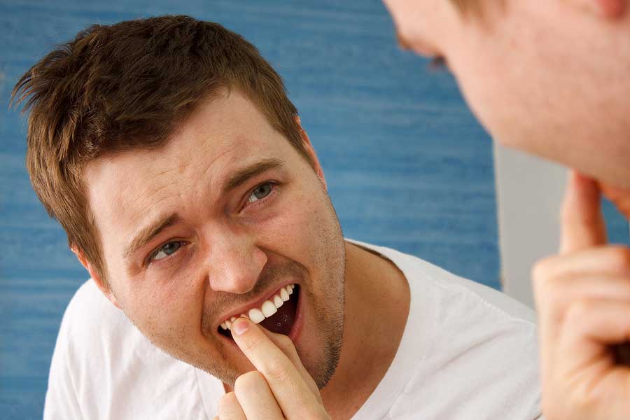 Man in a white tee, checking his tooth in the mirror